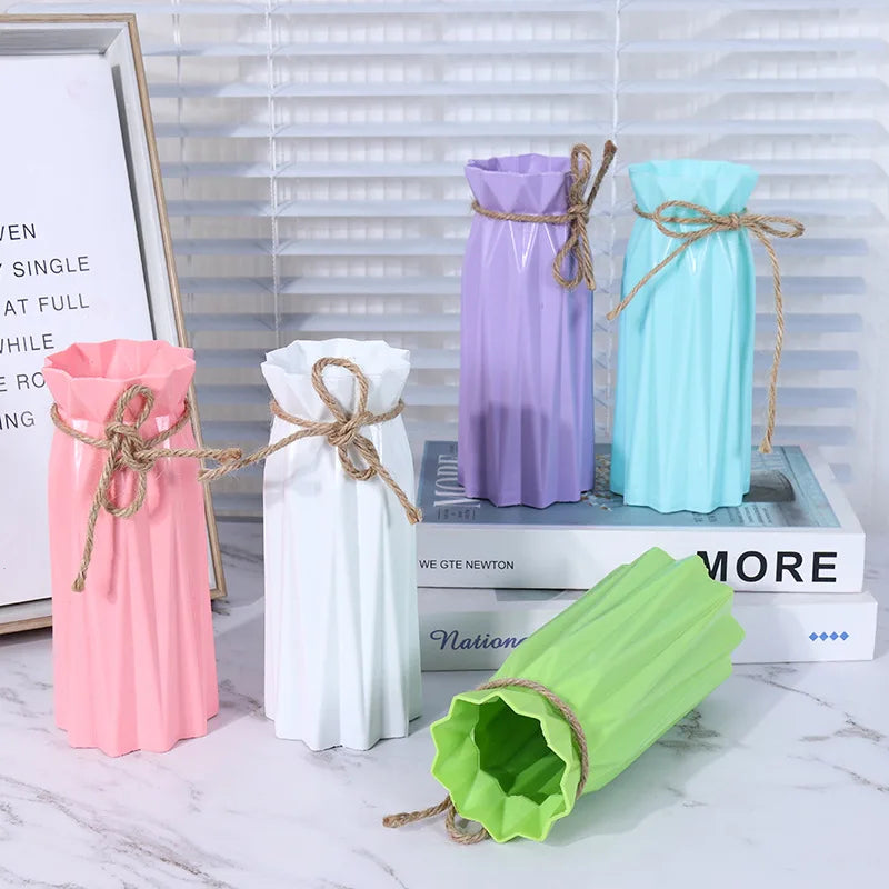 Three plastic vases in pink, white, and light blue with twine accents displayed on a marble surface.