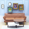 A brown leather sofa is positioned below a gallery wall featuring framed artwork of smiling women.