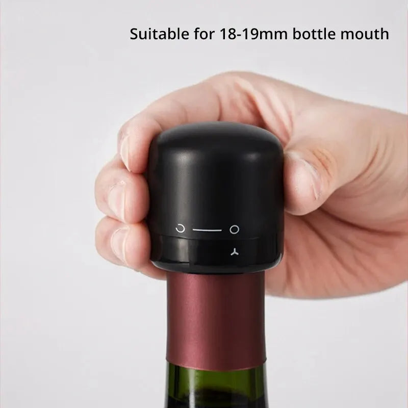 A hand holds a black silicone bottle stopper with a pink glass bottle neck.