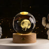 A clear glass crystal ball with a golden light inside rests on a wooden base against a dark background.
