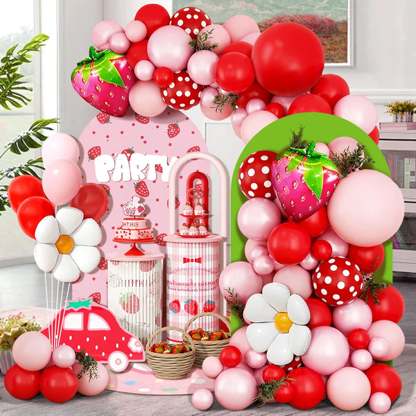 A colorful party decoration featuring a balloon arch wreath with pink, red, and white balloons and strawberry accents.