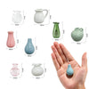 A collection of small ceramic plant vases in various shades of pink, green, and blue, shown next to a hand.