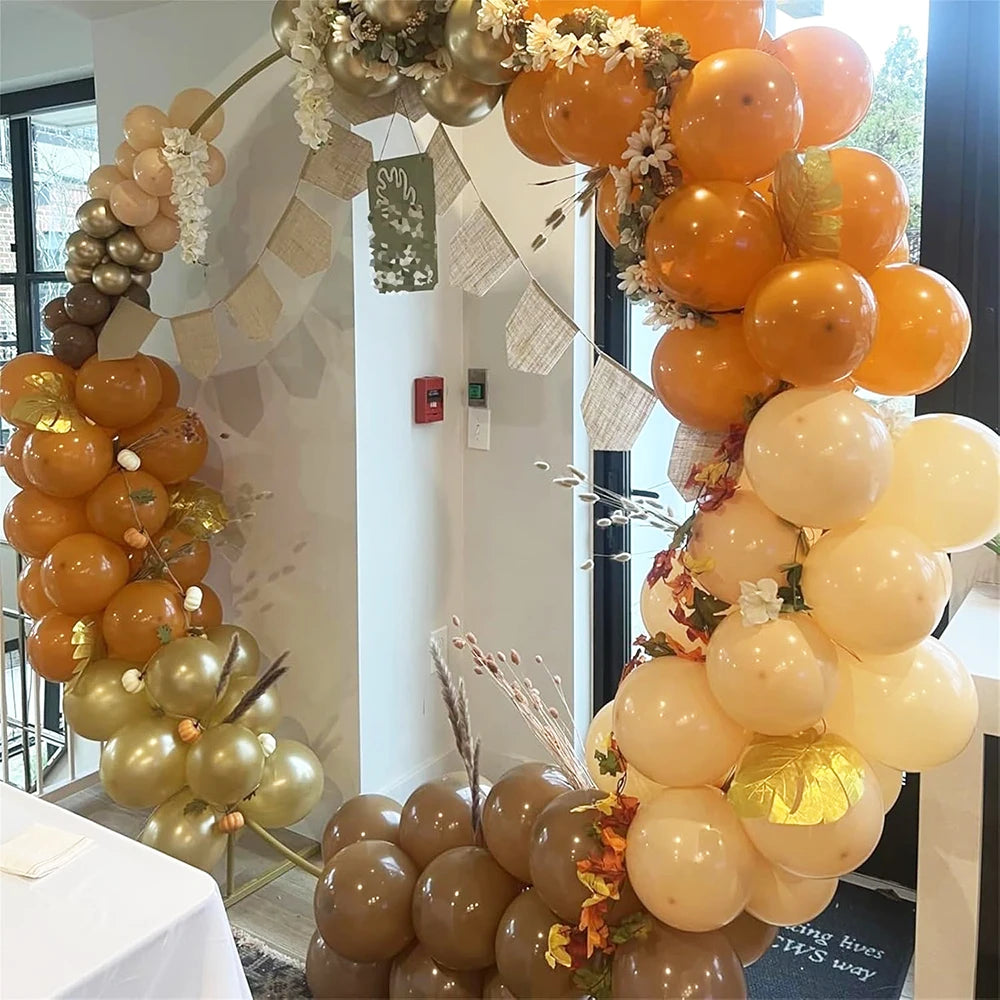 A garland of orange and gold latex balloons decorates a backdrop for an event.