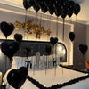 Black balloons with foil letters and rose petals hanging from the ceiling above a bed.