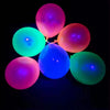 A cluster of glowing latex balloons in shades of pink, purple, and green against a black background.