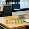 A set of six cute mini resin frog figurines in various shades of green and beige arranged on a wooden desk.
