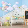 White crib decorated with cloud felt hanging decorations and balloons in a light blue room