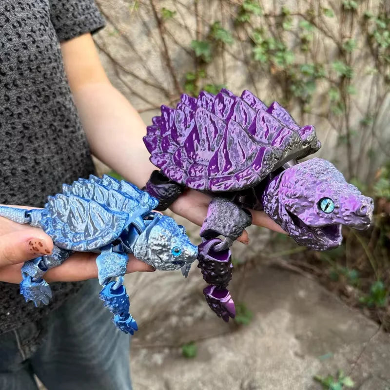 A hand holds a purple 3D printed alligator snapping turtle figurine with articulated joints against a blurred outdoor backgro