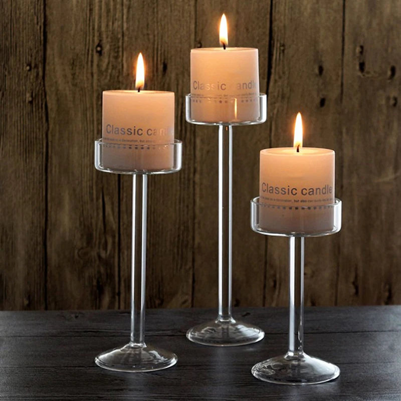 Three elegant tall glass candles with lit flames displayed on a dark wooden surface.