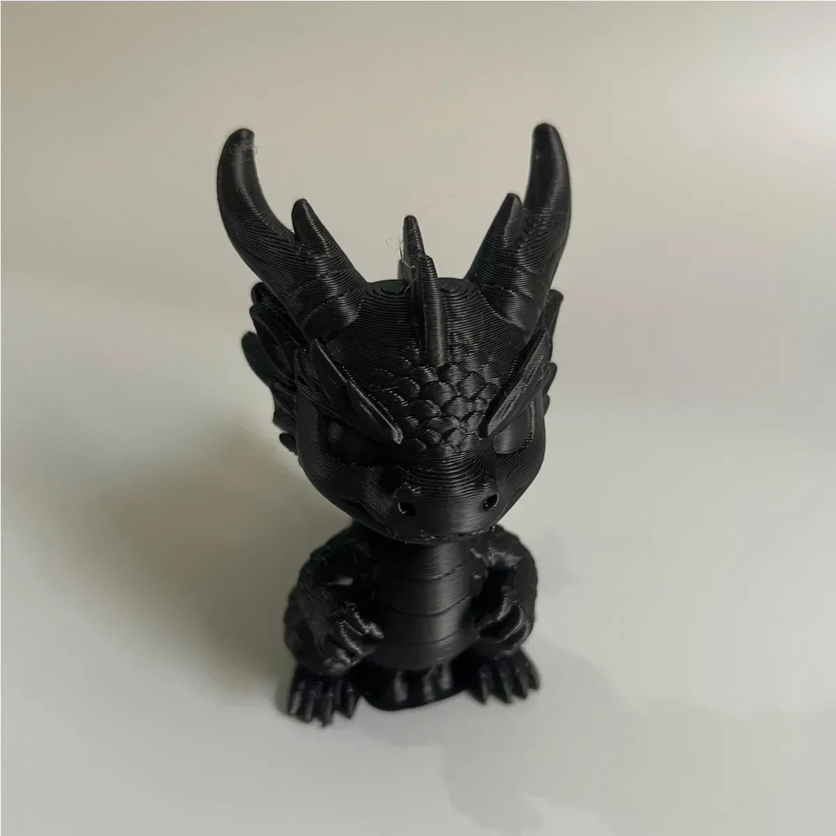 A black 3D printed mini dragon statue collectible with spiky horns sitting on a white surface.