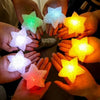 Several hands are holding glowing LED star lights of various colors, including green, white, purple, and yellow.