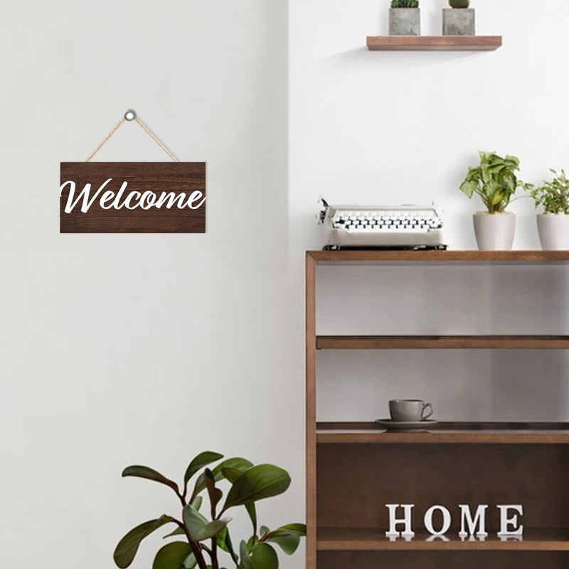 Rustic wooden welcome sign with the word Welcome mounted on a white wall above a wooden shelf.