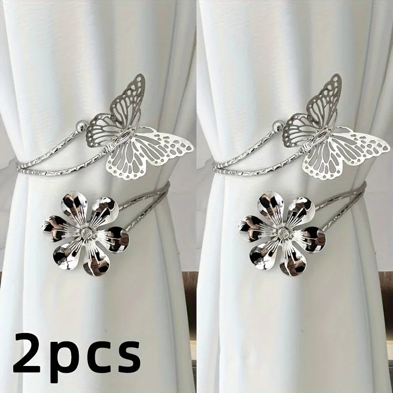 A set of two silver decorative flower butterfly curtain tiebacks displayed against a white curtain.