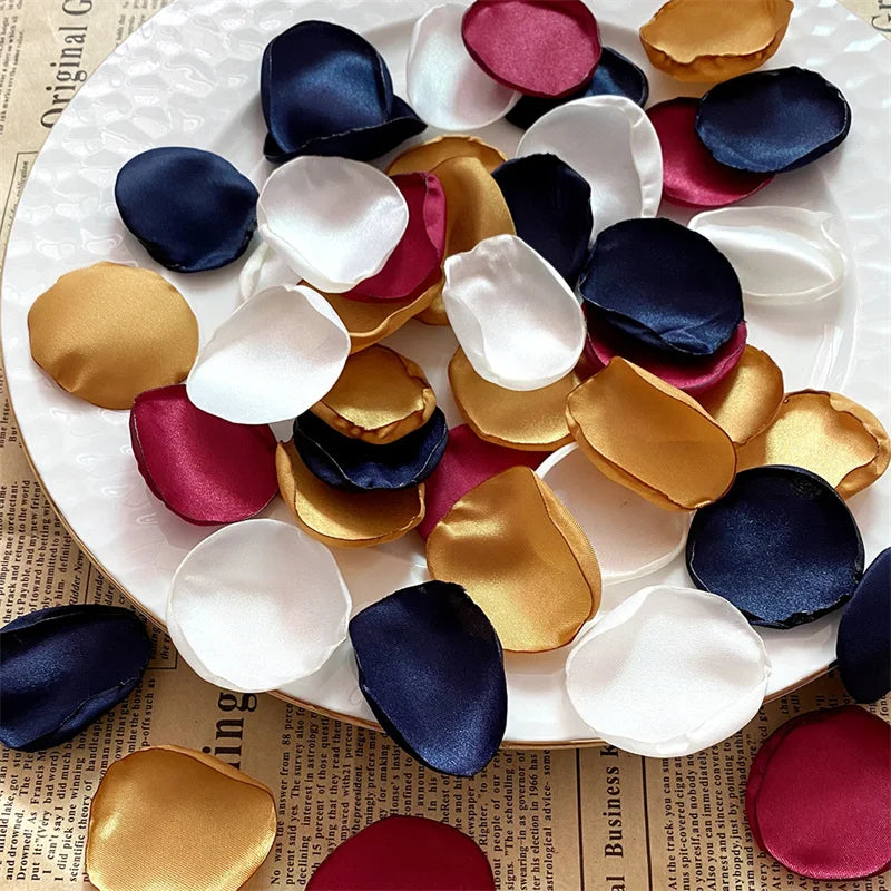 A collection of silk rose petals in shades of navy blue, deep pink, and gold arranged on a white plate.