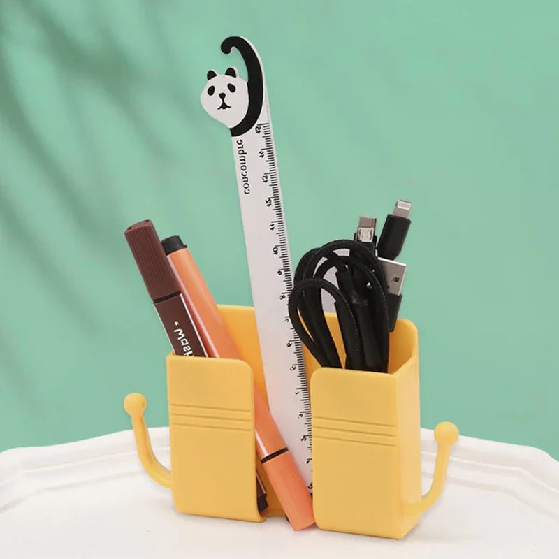 A yellow organizer holds a black cat-shaped ruler and various electronic accessories on a light green background.