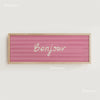 Pink striped canvas print with the word Bonjour written in white script on a light wood frame.