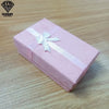 Una caja de regalo decorativa de joyería rosa atada con una cinta blanca, sobre una superficie de madera.