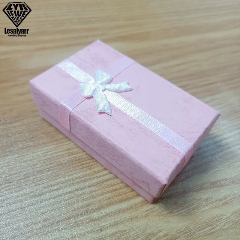 Una caja de regalo decorativa de joyería rosa atada con una cinta blanca, sobre una superficie de madera.