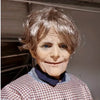 A close-up photo of a person wearing a realistic cute alien full-face latex mask with blue eyes and wrinkled features.