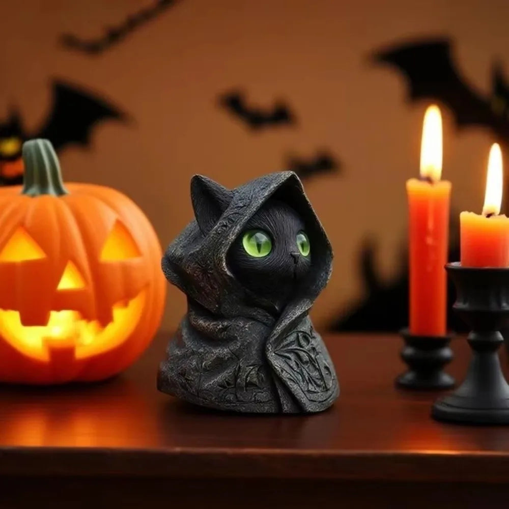 A dark gray gothic hooded cat statue sits on a wooden surface next to an orange pumpkin and lit candles.