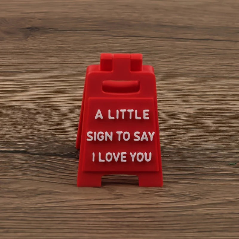 A red plastic sign with the text A LITTLE SIGN TO SAY I LOVE YOU engraved on it.