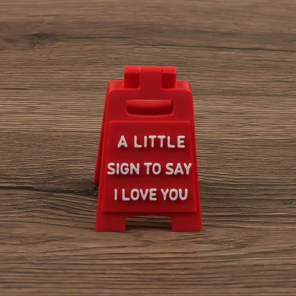 A red plastic sign with the text A LITTLE SIGN TO SAY I LOVE YOU engraved on it.