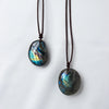 A dark blue and green labradorite gemstone pendant on a dark brown leather cord.