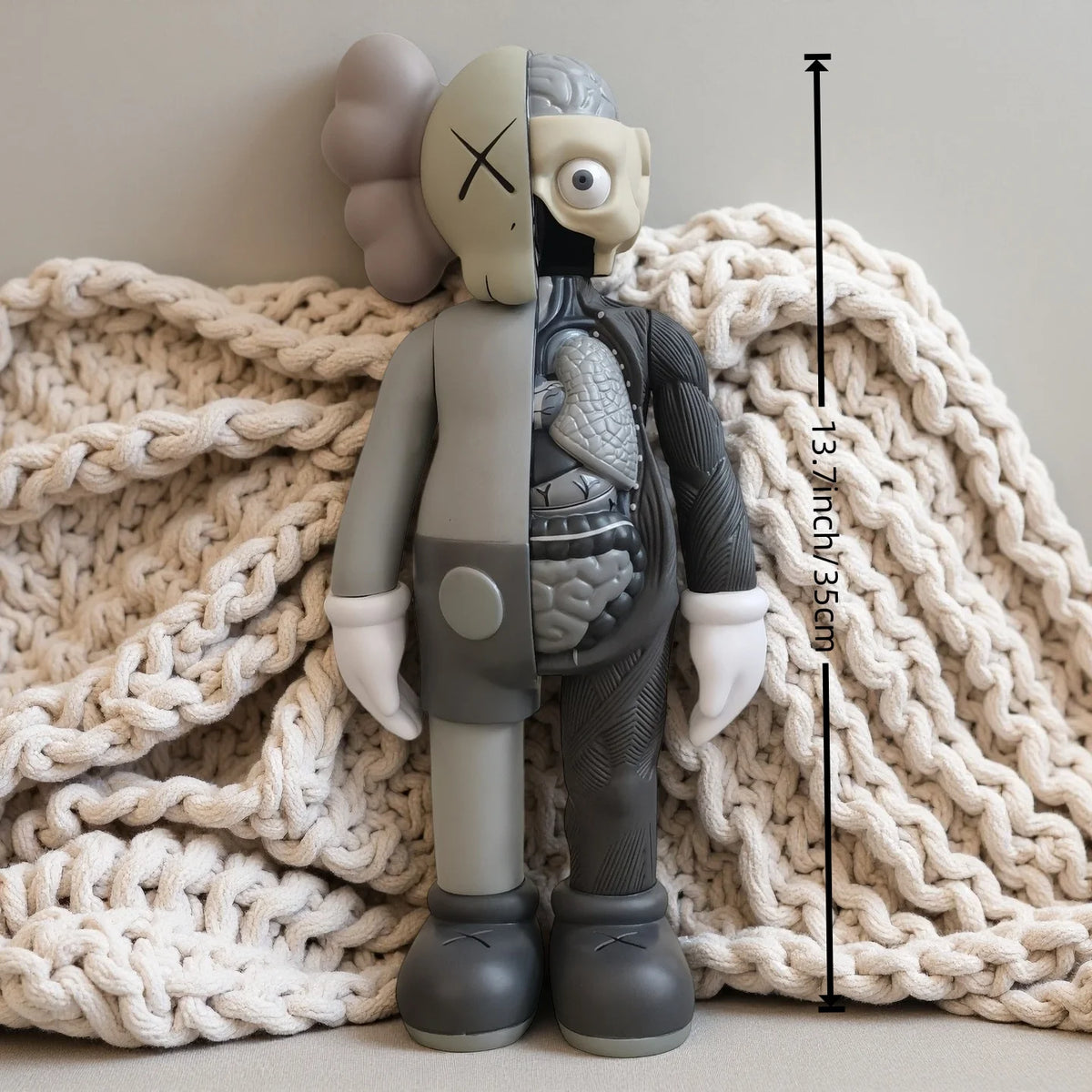 A gray and beige Kawaii bear figurine standing on a cream knitted fabric.