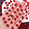 A hand displays a collection of red and black ladybug resin nail art charms.