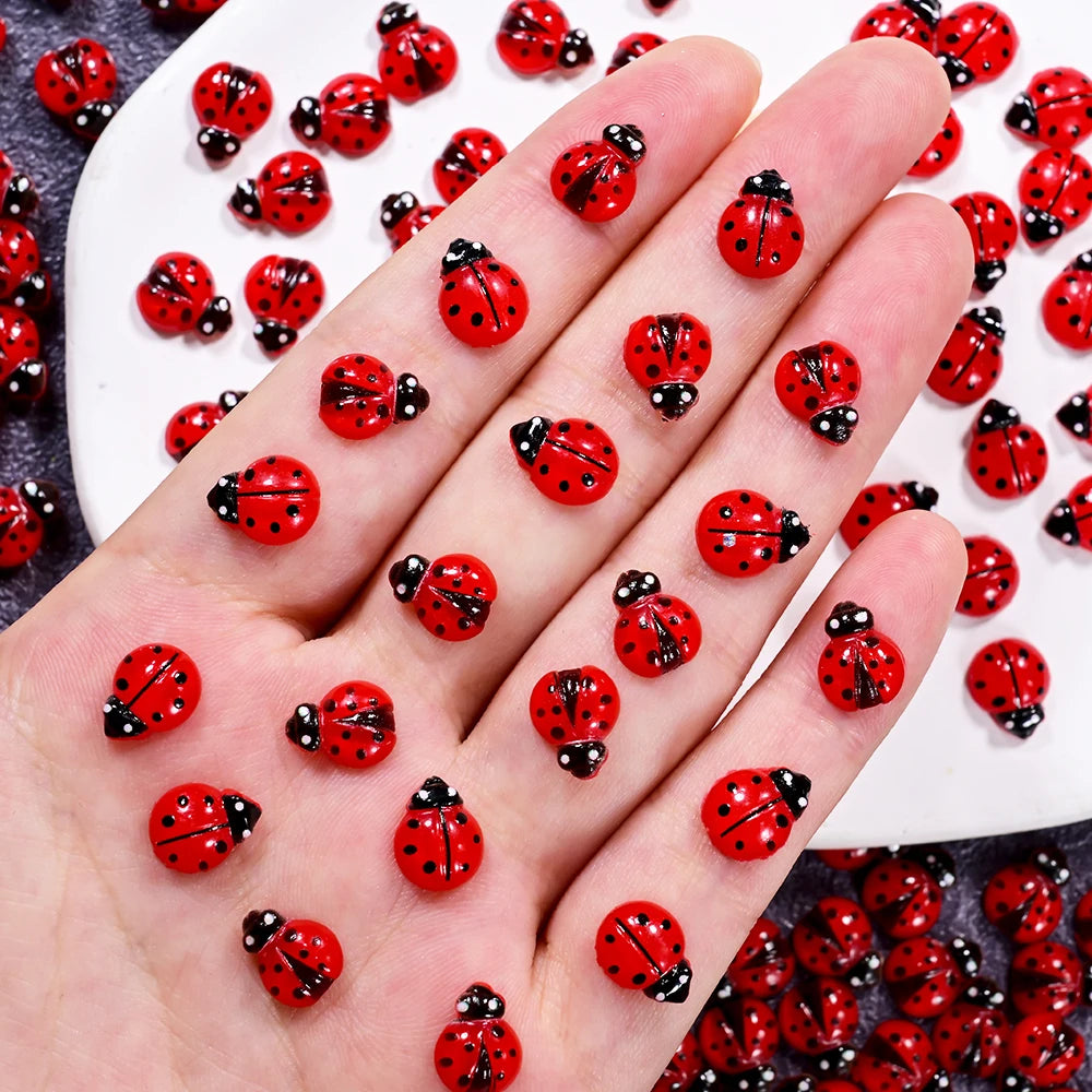 A hand displays a collection of red and black ladybug resin nail art charms.