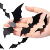 A hand holds several black 3D bat wall stickers for Halloween decor.