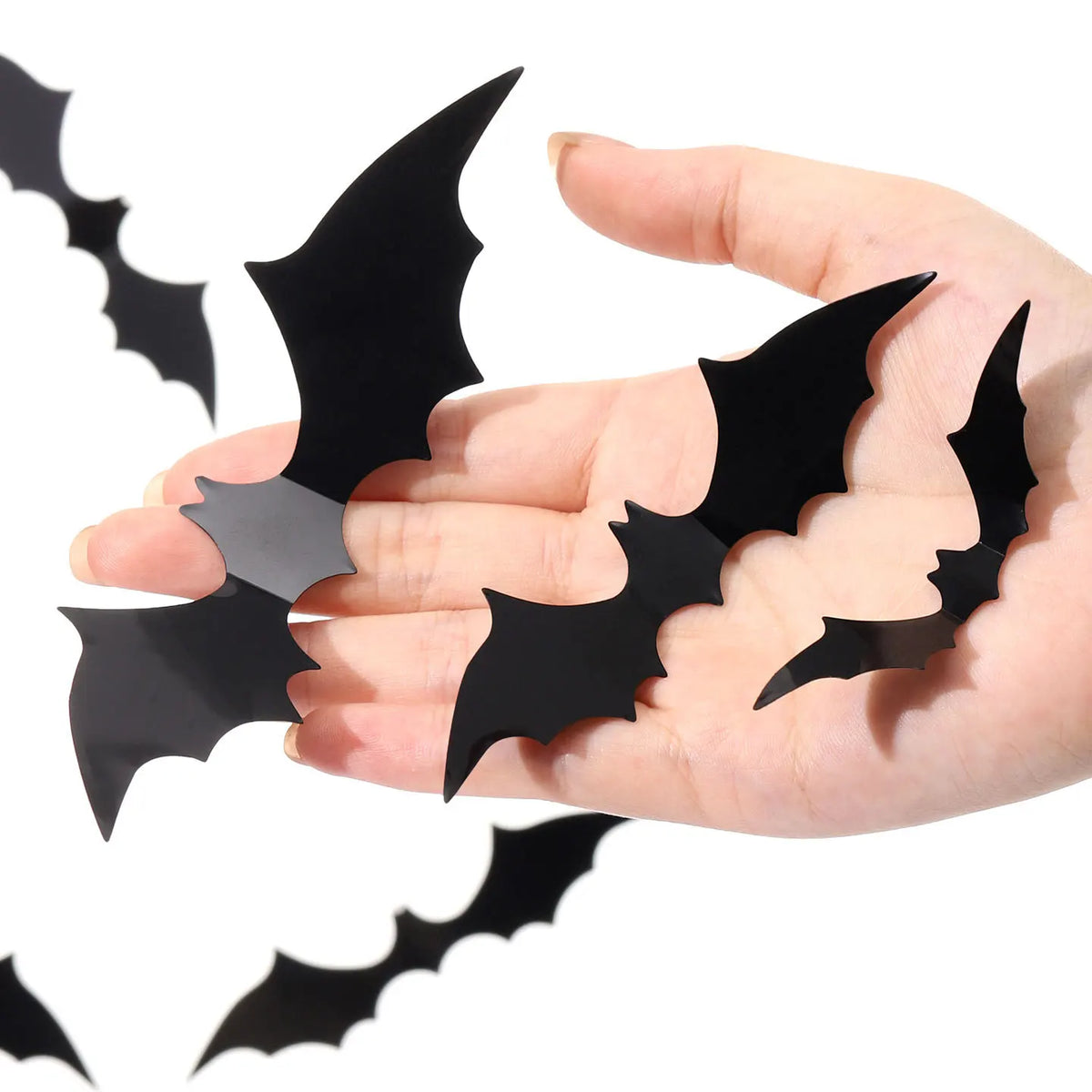 A hand holds several black 3D bat wall stickers for Halloween decor.