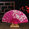 A pink folding fan decorated with white plum blossoms, displayed on a wooden stand.