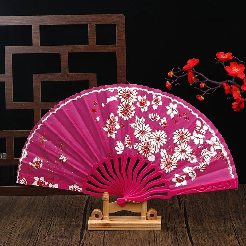 A pink folding fan decorated with white plum blossoms, displayed on a wooden stand.