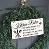 A wooden hanging sign with kitchen rules written on it, displayed on a green faux garland.