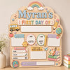 A wooden sign for a child's first day of school featuring illustrations like a school bus, rainbow, and various labels.