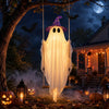 Una decoración fantasma de tela blanca brillante cuelga de una rama bajo una luna llena con murciélagos y calabazas de fondo.