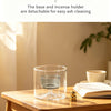 A clear glass incense burner with a gourd shape and a removable base sitting on a wooden table.