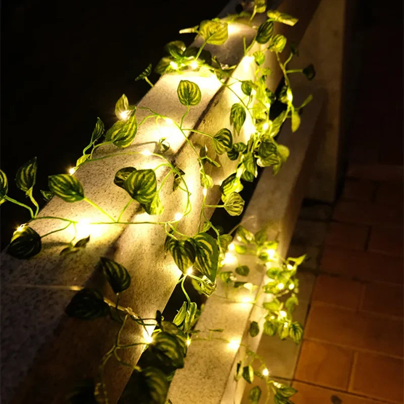 String lights with artificial leaves illuminate a stone railing at night.