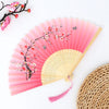 Pink and white floral patterned vintage bamboo folding fan resting on a woven mat.