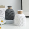 A white plastic vase with a textured ripple pattern and a natural fiber lid sits next to a dark gray ceramic vase.