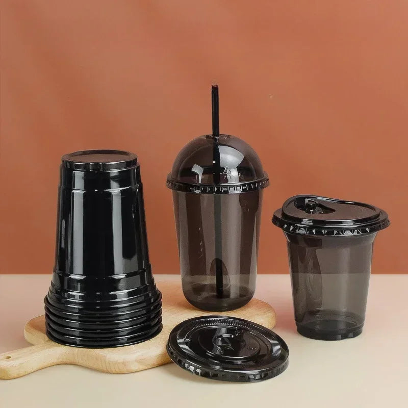 A set of black disposable U-shaped coffee cups and a lid displayed on a light wooden surface against a terracotta background.