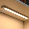 A long, linear LED light fixture with a motion sensor is mounted under a cabinet in a beige kitchen setting.