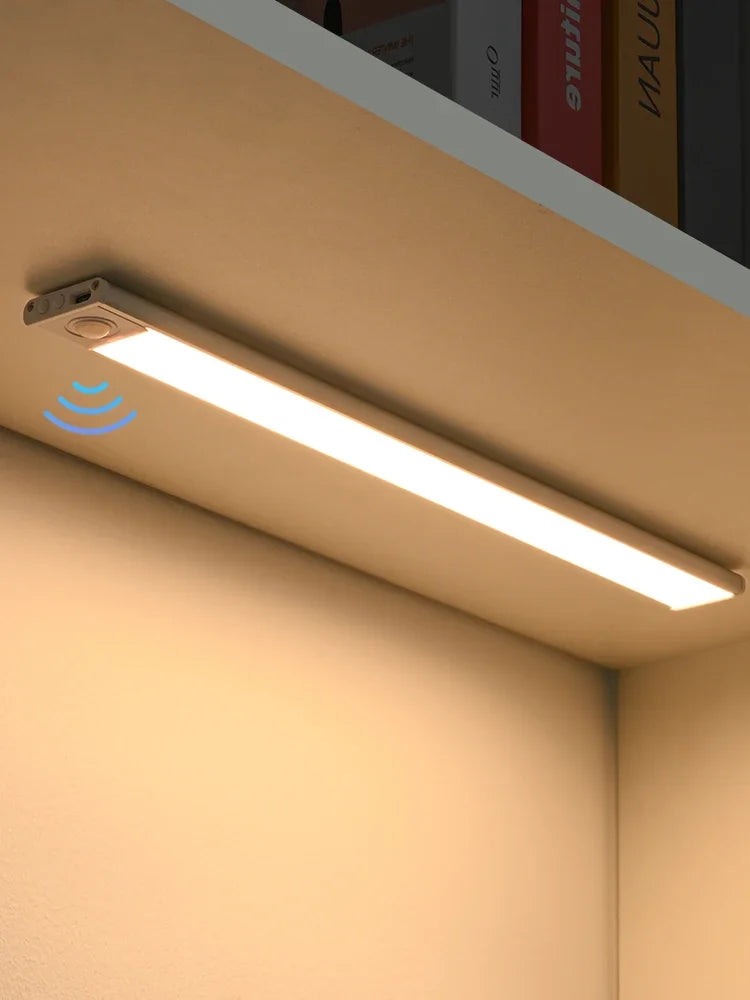 A long, linear LED light fixture with a motion sensor is mounted under a cabinet in a beige kitchen setting.