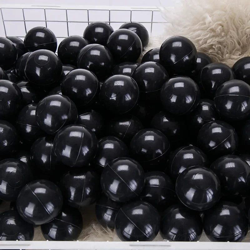 A large pile of black, glossy, spherical ocean balls for kids is displayed in a white basket.