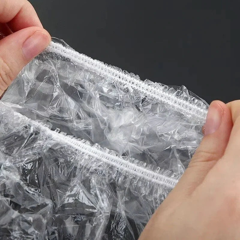 A hand is holding a clear reusable plastic food wrap cover with an elastic edge.