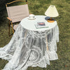 Elegant white floral lace tablecloth covering a round table outdoors with a light lamp.