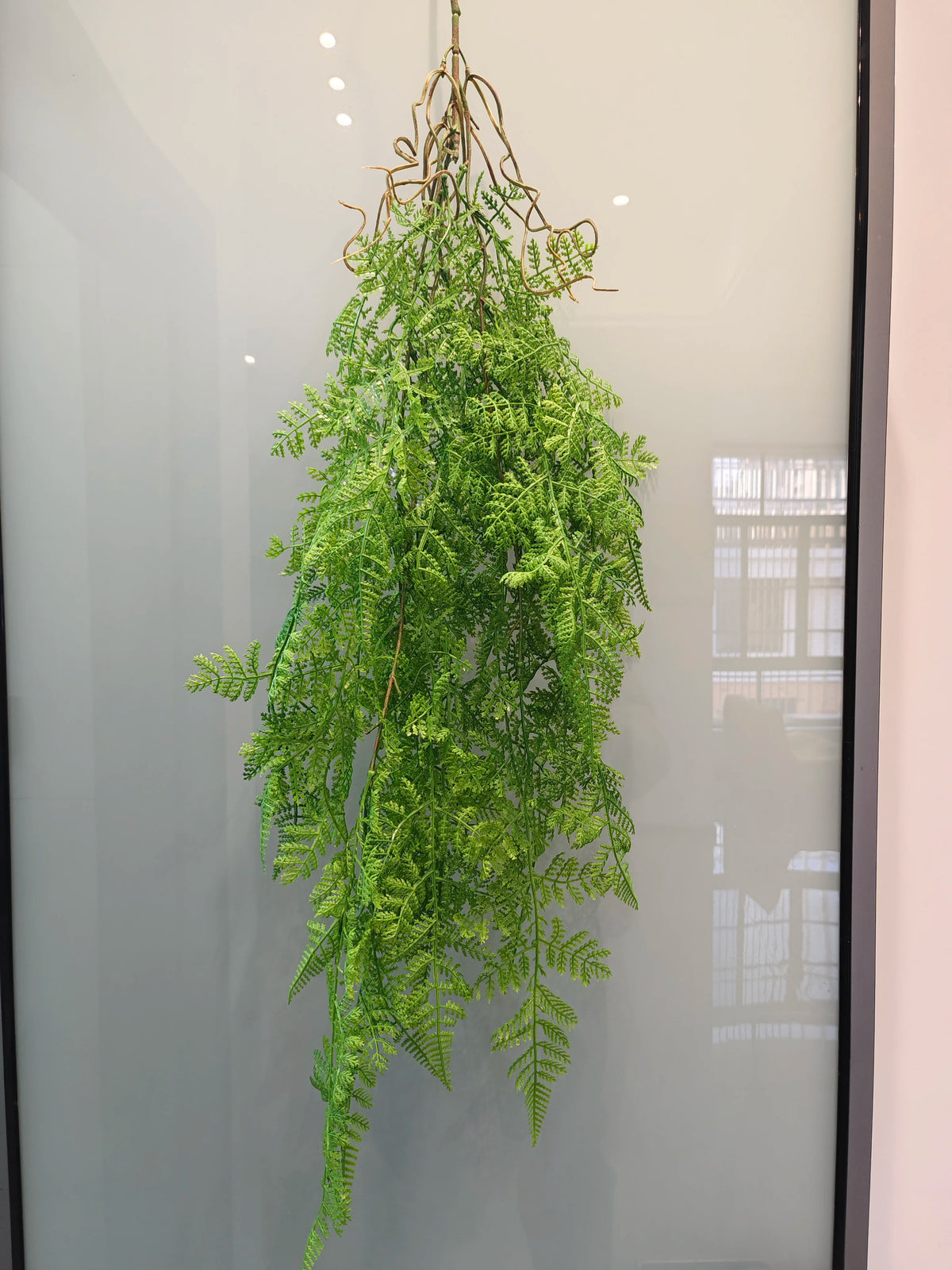 Artificial hanging ivy vine with green leaves displayed in a glass cabinet.