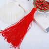 Red silk tassel with a gold coin knot decoration placed next to a white seashell on a book.