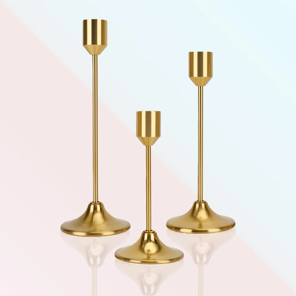 A set of three modern gold metal taper candle holders with flared bases and slender stems.